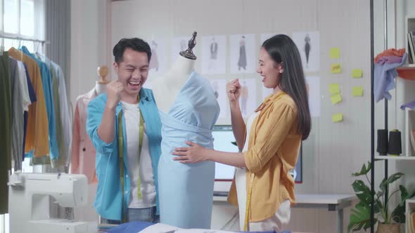 Happy Asian Male And Female Designers Celebrating Succeed Wearing Fabric On A Mannequin