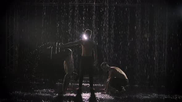 Silhouettes of Three Athletic Men Performing Acrobatic Stunts in the Rain. Artists in the Spotlight