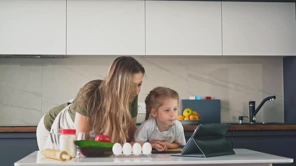 Girl and Mother Watch Food Video Blog at Table in Kitchen