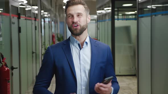 Excited Young Businessman Rejoices at Message on His Smartphone Standing at Office