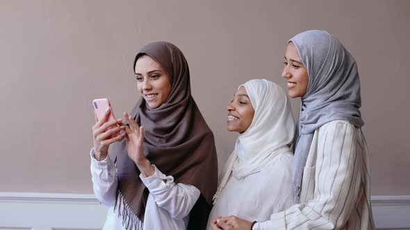 Three Muslim Girls Taking Selfie on the Phone Smiling in Beige Studio