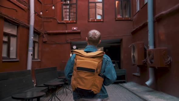 Rear View of a Young Male Traveller Walking Around the City with Yellow Backpack and Taking Photos