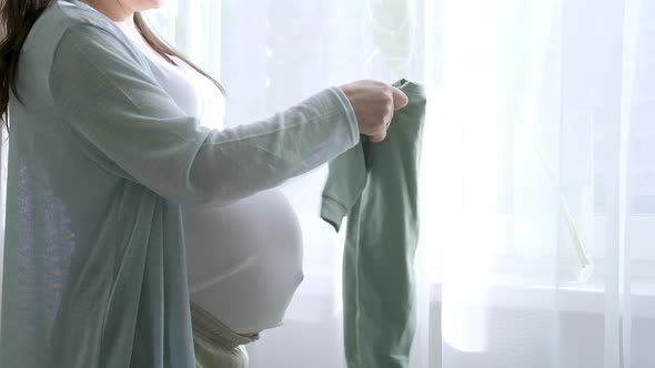 Pregnant Mother Holding Baby Clothes in Hands