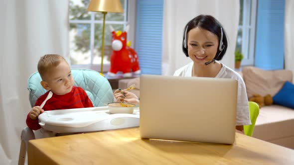 Young Woman Feeding Child and Having Video Call on Laptop