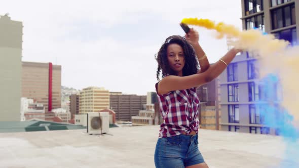 Fashionable young woman on urban rooftop using smoke grenades