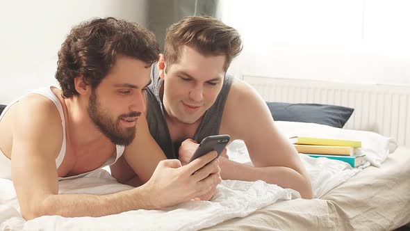 Attractive Male Gay Couple Uses Smartphone in Home.