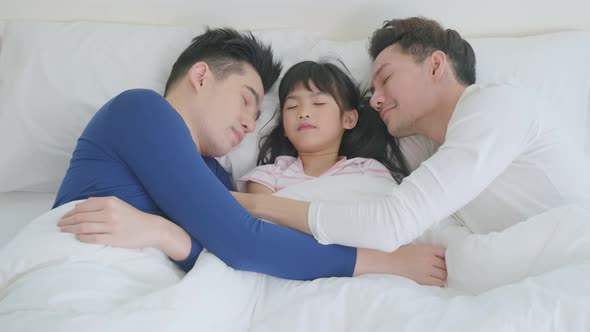 Asian handsome man gay lying down on bed with husband couple and kid daughter in bedroom at home.