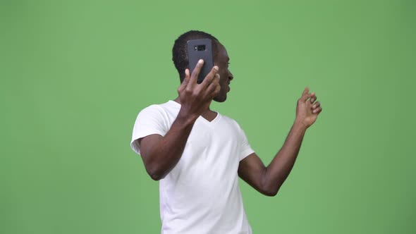 Young African Man Video Calling with Phone Against Green Background