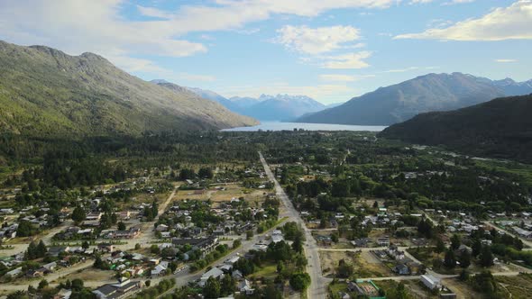 Dolly out flying over Lago Puelo village surrounded by pine tree woods with lake and Andean mountain