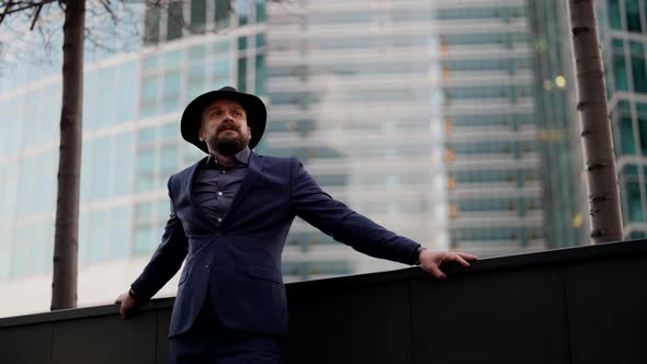 a Bearded and Mustachioed Stylish Man in a Plaid Suit Leaned Hands on the Parapet and Then Takes Off