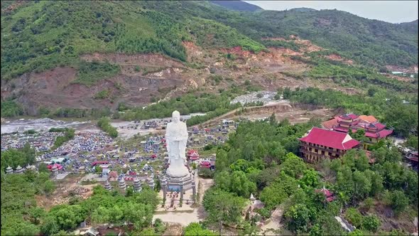 Flycam Approaches Large Buddha Statue By Temple Against Hills