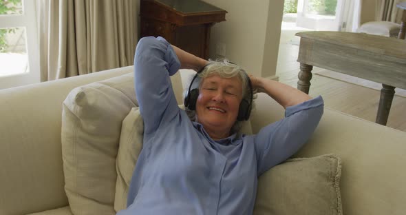 Caucasian senior woman wearing headphones smiling while listening to music at home