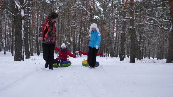 Happy Dad and Mom Pull Sleds with Children in Winter Forest. Parents Play with Children in a Snowy Park