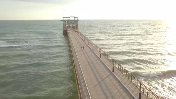 Aerial view of teen couple boy and girl walk by hand on pier in sea at sunset. Summer vacation, love