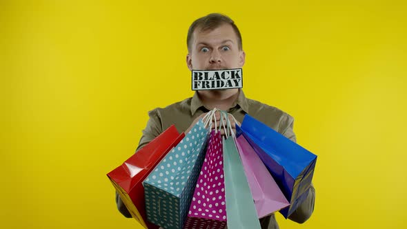 Surprised Man Showing Shopping Bags and Black Friday Inscription in His Mouth, Yellow Background