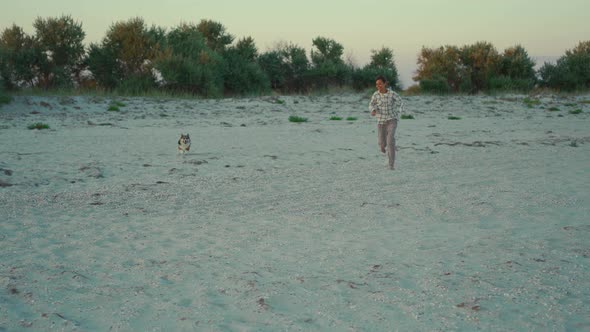 Happy Laughing Woman Getting Funand Running with Her Cute Welsh Corgi Dog on Sandy Beach at Sunset