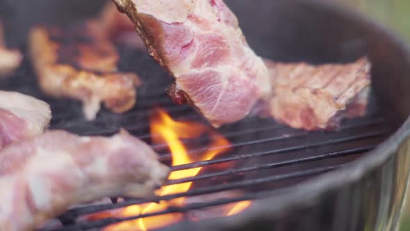 Slow Motion of Tongs Flipping Sizzling Meat on Fiery and Smokey BBQ Grill