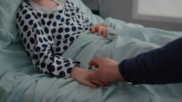 Close Up of Father Sitting with Sick Daughter in Hospital Ward Holding Hands