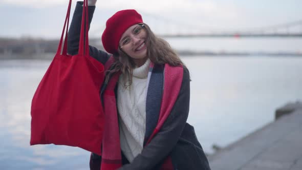 Happy Young Woman with Toothy Smile Showing New Red Bag Looking at Camera Smiling