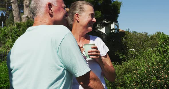 Caucasian senior couple holding coffee cup talking to each other in the balcony at home