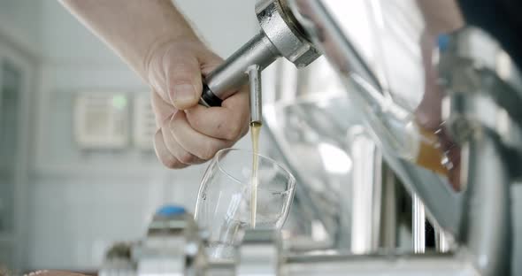 Slow Motion. Brewery Worker Pouring Fresh Craft Beer From Tap of Steel Vat Into Glass. Close Up.