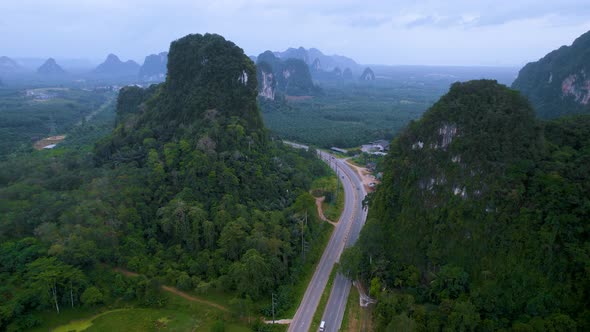 Aerial View of the Road with Driving Cars and Trucks Between High Cliffs Mountains with Jungle Palm