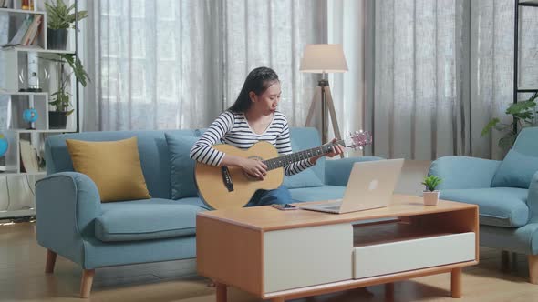 Asian Woman Having Video Call On Laptop And Playing A Guitar At Home