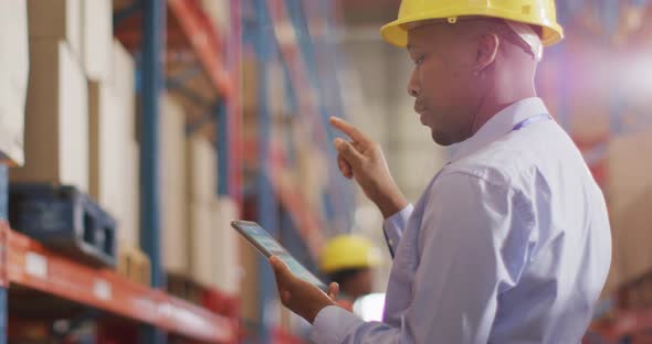 African american male worker with helmet using smartphone in warehouse