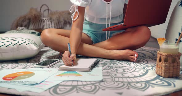 Freelance Woman She Sits on the Carpet and Types on Lap Top Computer and Writes Notes Into Notepad