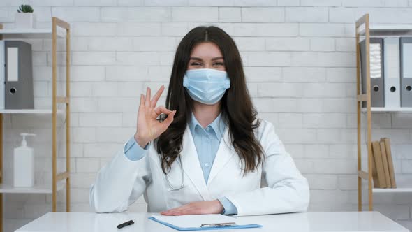 Female Doctor Gesturing Okay Wearing Protective Face Mask In Office