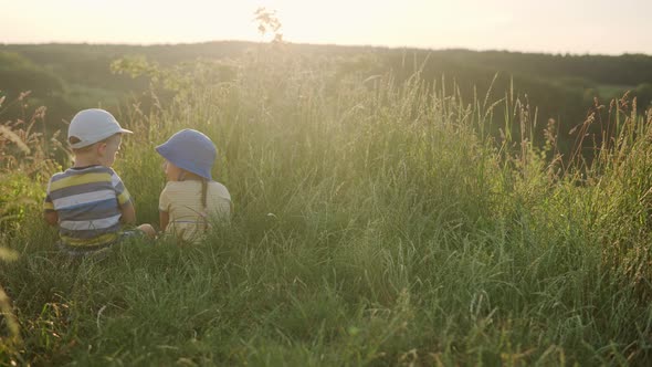 Cute Preschool Little Baby Girl and Boy Sitting on Top of Mountain in Tall Grass Before Sunset