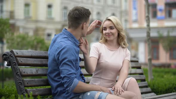 Young Couple Sitting on Bench, Guy Looking at Girl and Caressing Her, Tenderness