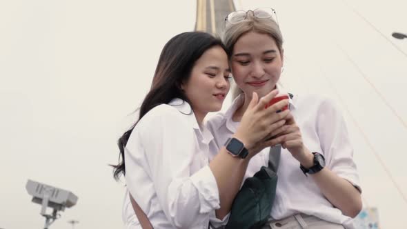 Asian lesbian couples using smartphones browsing the website while standing on the bridge.