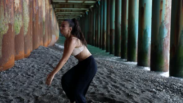 Passionate Woman is Dancing on Sea Coast Under Pier Moving Her Body Sexually and Looking at Camera