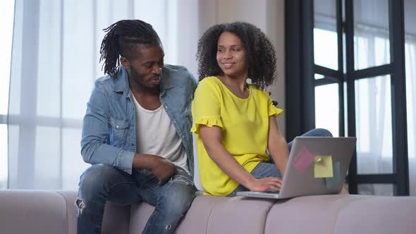 Loving Young African American Husband Hugging Confident Wife Working Online From Home