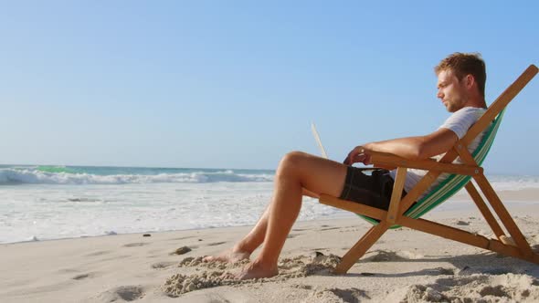 Man using laptop at beach in the sunshine 4k