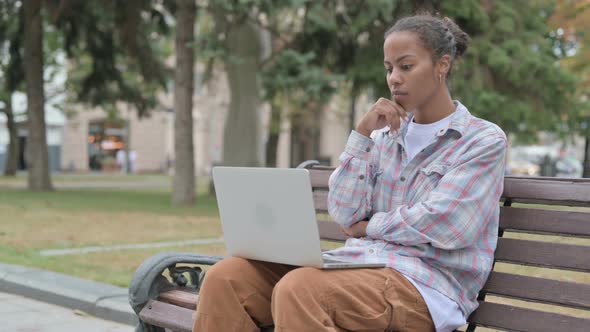 Thinking African Woman Using Laptop While Sitting Outdoor on Bench