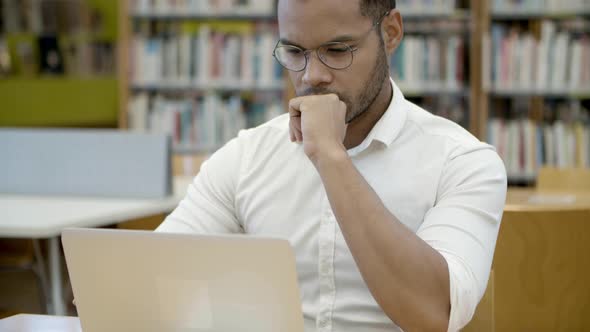 Focused Young Man Working with Laptop in Library