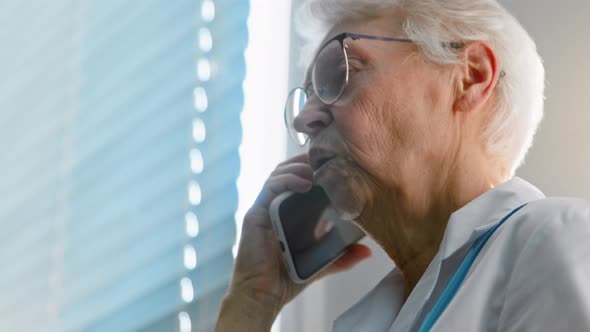 Mature lady doctor with glasses talks on mobile phone giving recommendations to patient