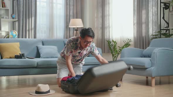 Asian Man Preparing For Travel Adventure, Packing Clothes Into Suitcase, Getting Ready For Road Trip