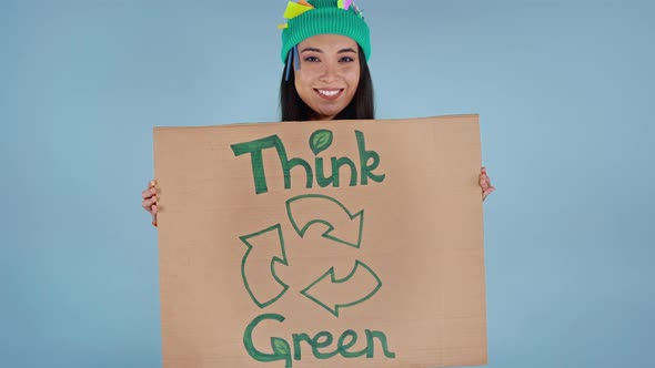 Woman holding cardboard poster with isncription think green on it.