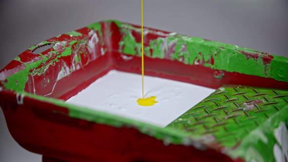 A Person Pouring Yellow Paint in the Paint Tray with White Paint