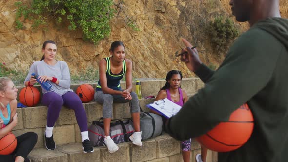 Diverse female basketball team and male coach discussing game tactics