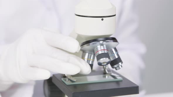 Closeup Researcher in Medical Gloves Works with Microscope in White Laboratory