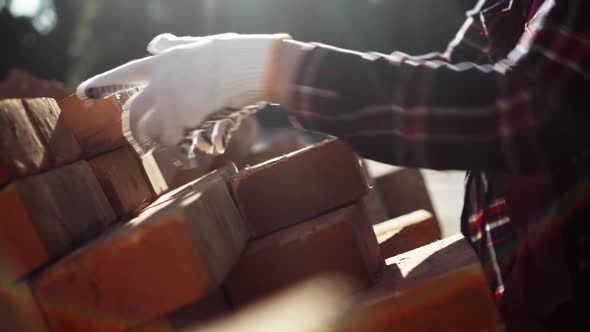 Builder's Hands Are Stacking Red Bricks In A Large Warehouse. Pile Of Building Material Bricks