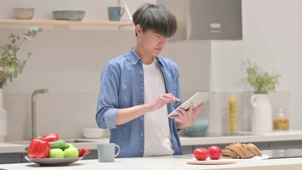 Young Asian Man Using Tablet While Standing in Kitchen