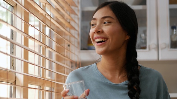 Close Up face Asian woman smiling and drinking water beside a window at home.