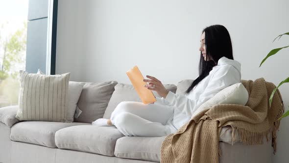 Young Woman Reading a Book While Sitting on a Sofa in a Living Room, Reading Books. Stay Home