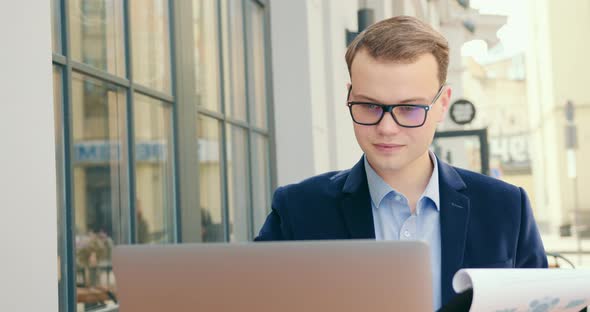 A Businessman Is Sitting at a Table in a Cafe and Working