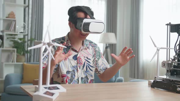 Asian Man Wearing Vr Glasses While Experimenting With Wind Turbine Model And 3D Printer At Home